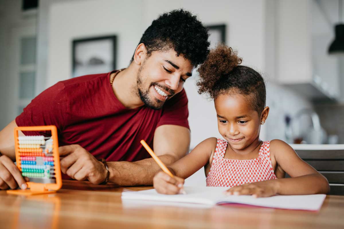 Father and daughter sit at a table with abacus and notebook