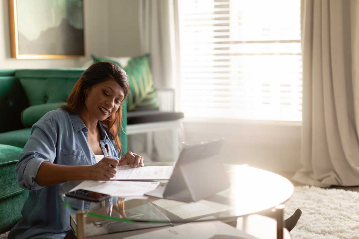 woman sits at coffee table with pen and paper and laptop