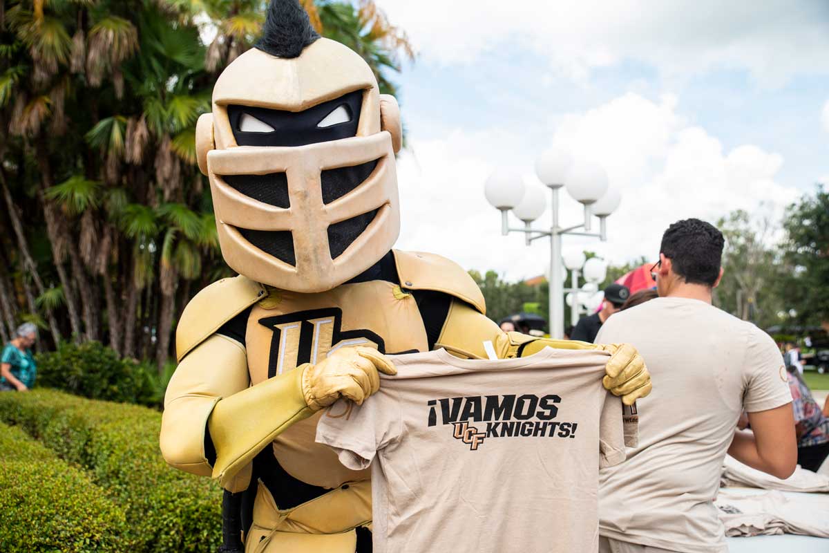 Knightro holds up Vamos Knights T shirt