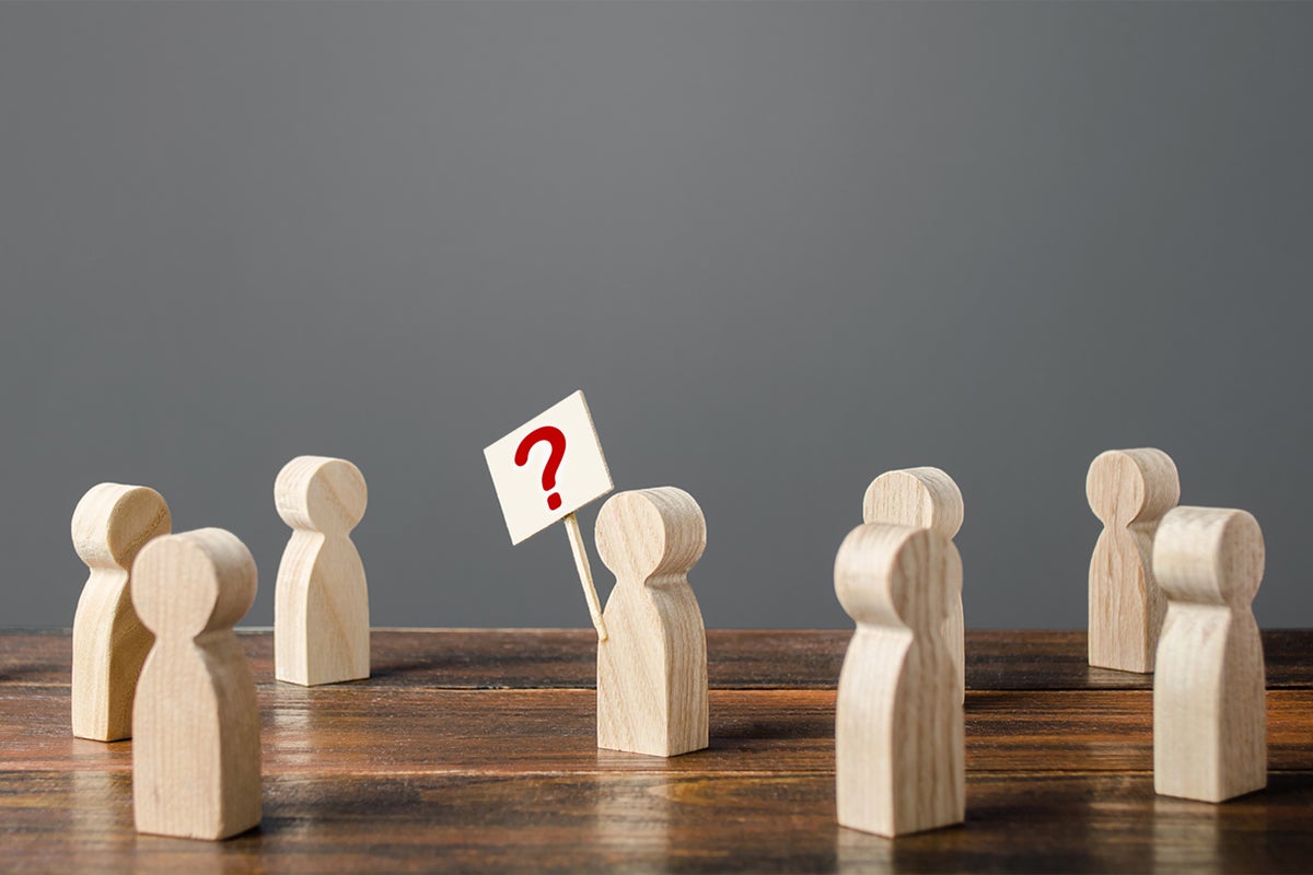 wooden people with one holding a protest sign with a question mark