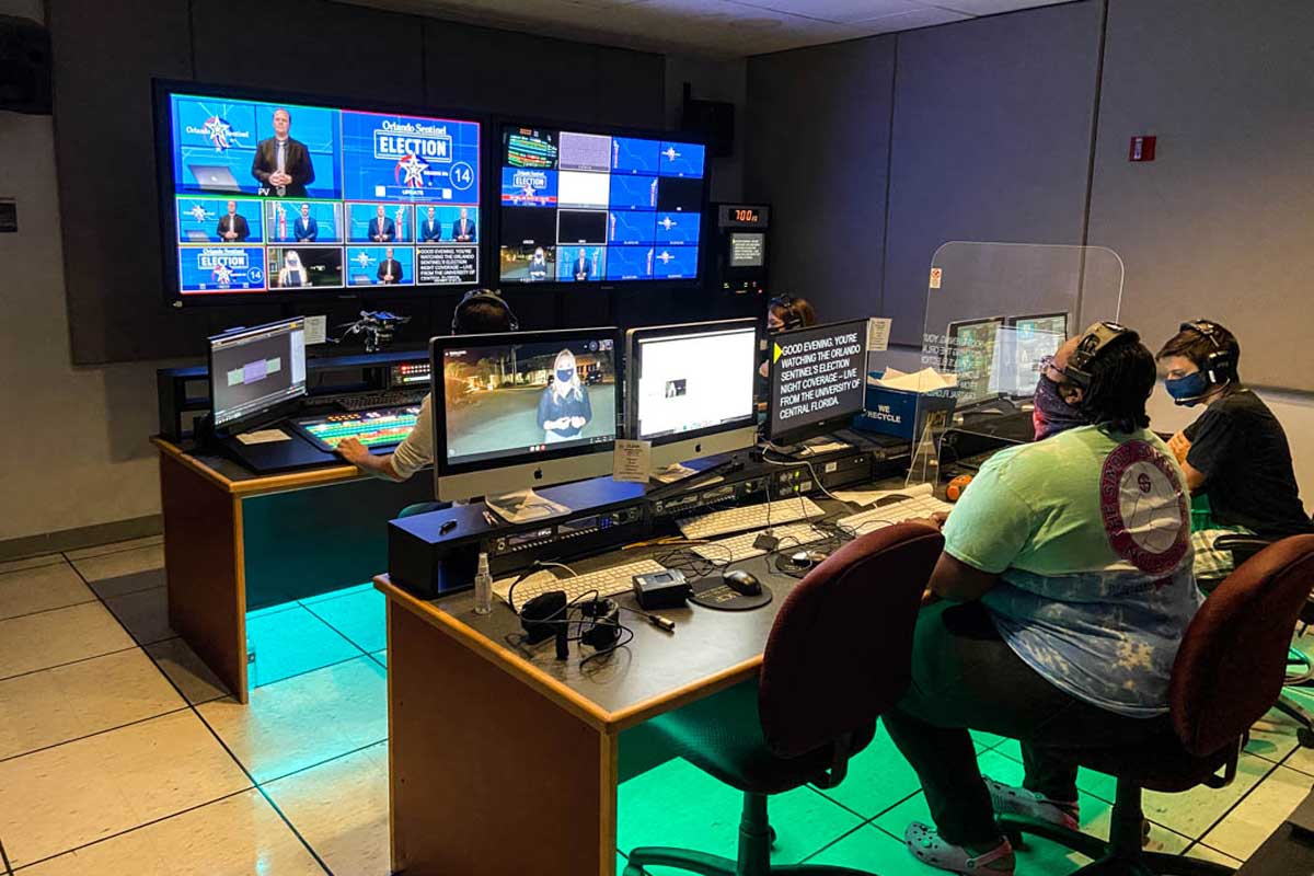 Two people sit in a room with desks and TVs mounted to wall