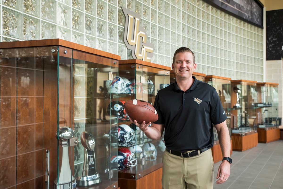 Danny White holds football in front of trophy cases