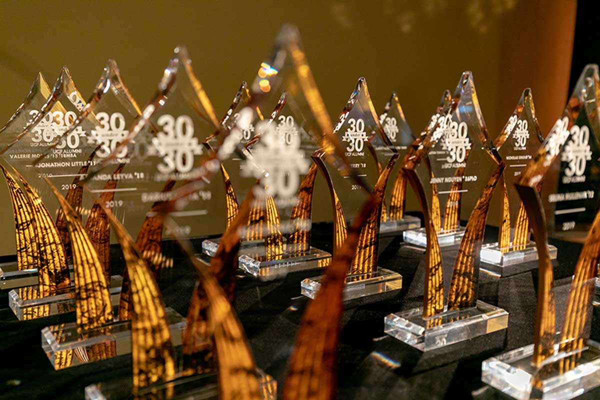 Glass awards in the shape of diamonds are in front of a yellow background. The awards say 30 Under 30 in white text.