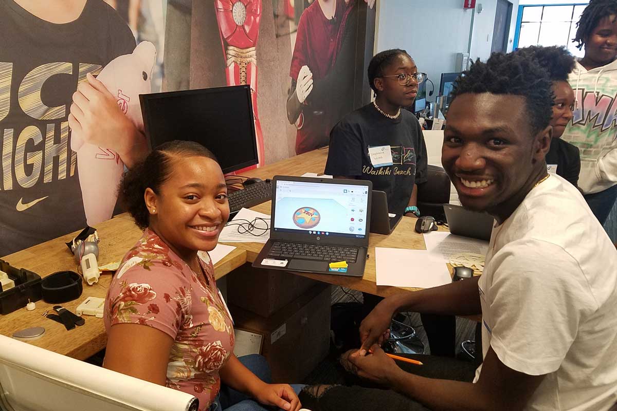 Students sit next to a computer and smile