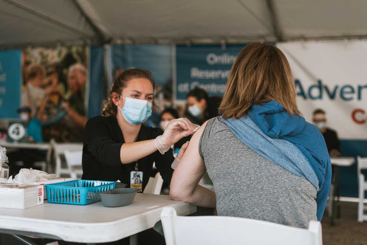 Woman wearing face mask preps a patient's arm for vaccination