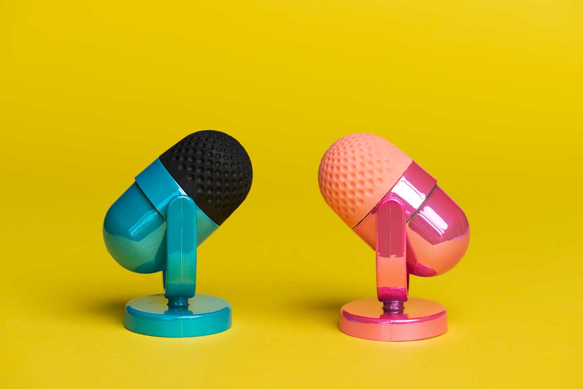 Two microphones facing each other. One microphone is pink the other microphone is blue on yellow background.