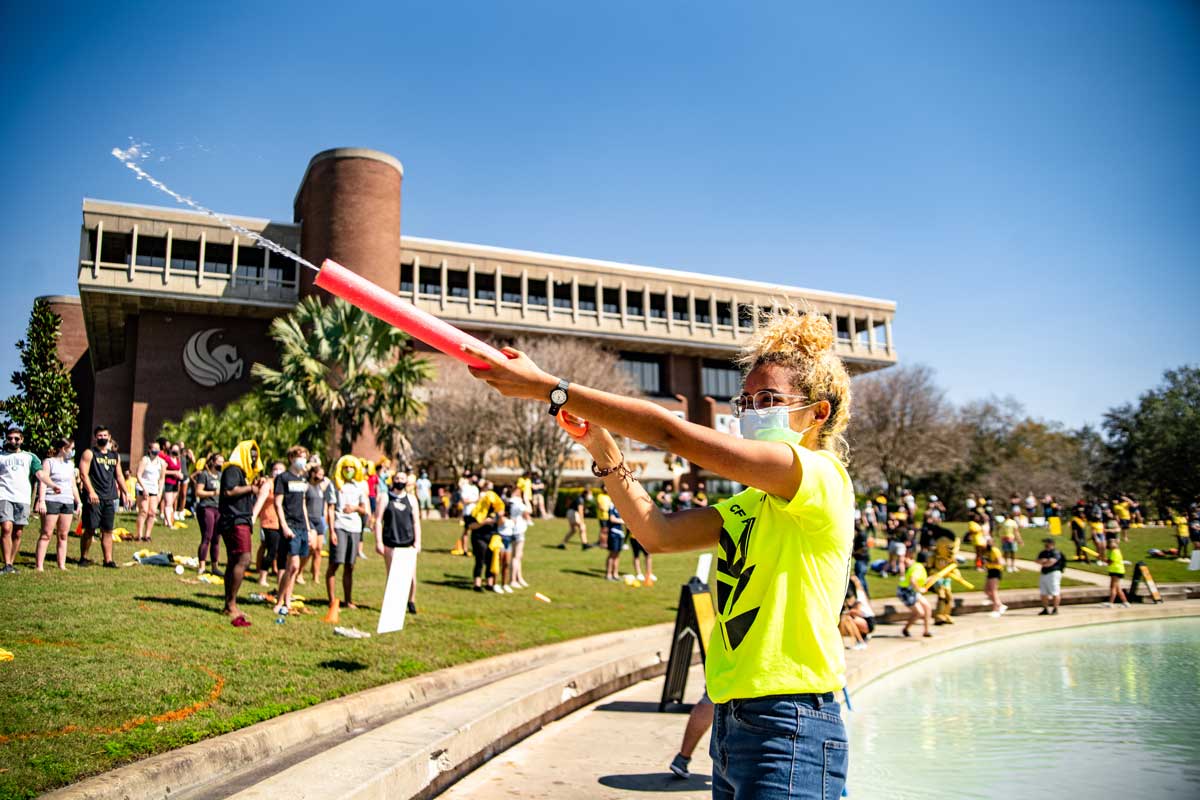 Young woman wearing bright neon yellow shirt aims squirt gun