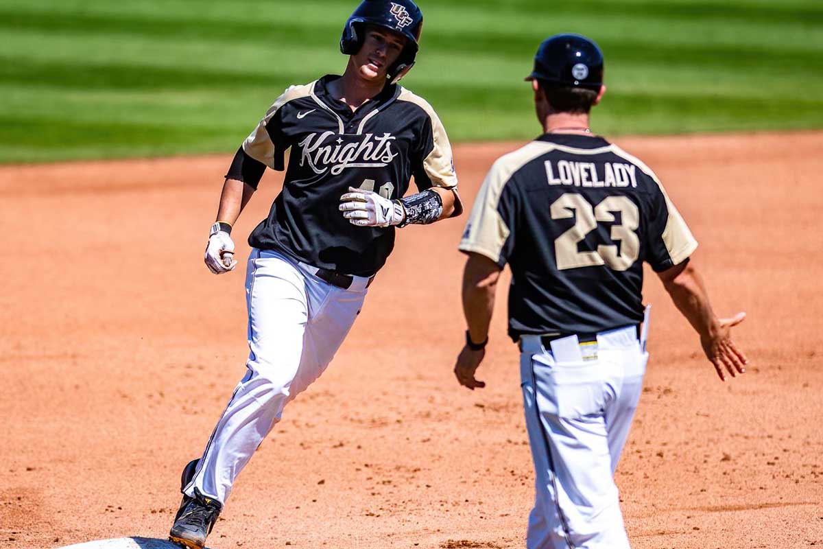 Baseball player rounds the base as UCF head coach Greg Lovelady extends his hand.