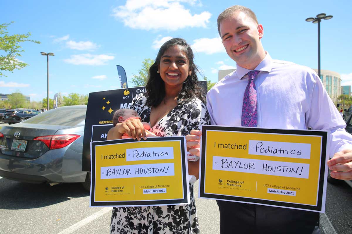 Two med students hold up yellow signs that say where they are headed for residencies