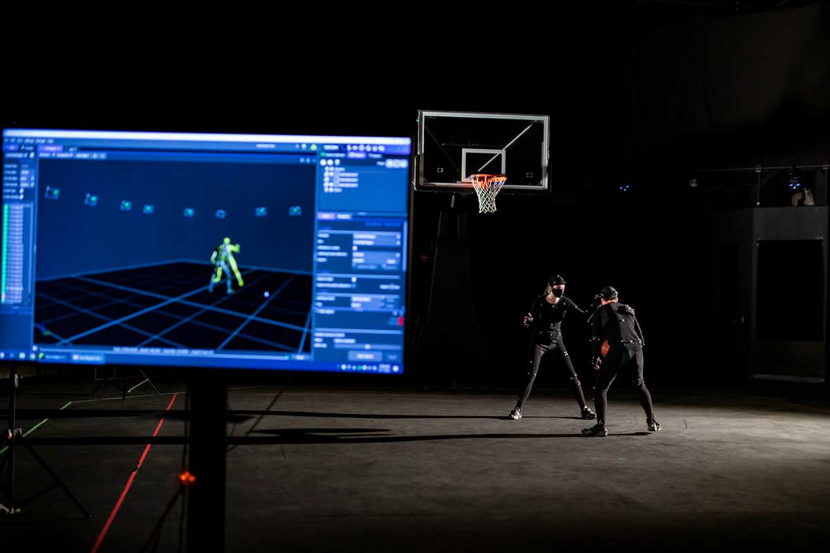 Two men wearing black motion sensor suits play basketball