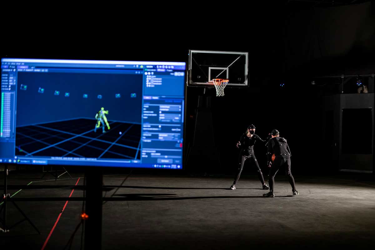Two men wearing black motion sensor suits play basketball