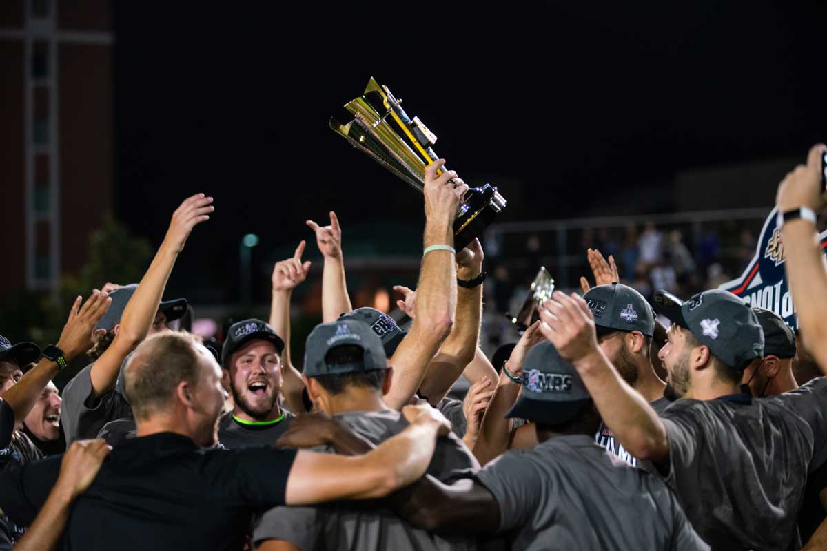 men's soccer team huddles with trophy raised overhead