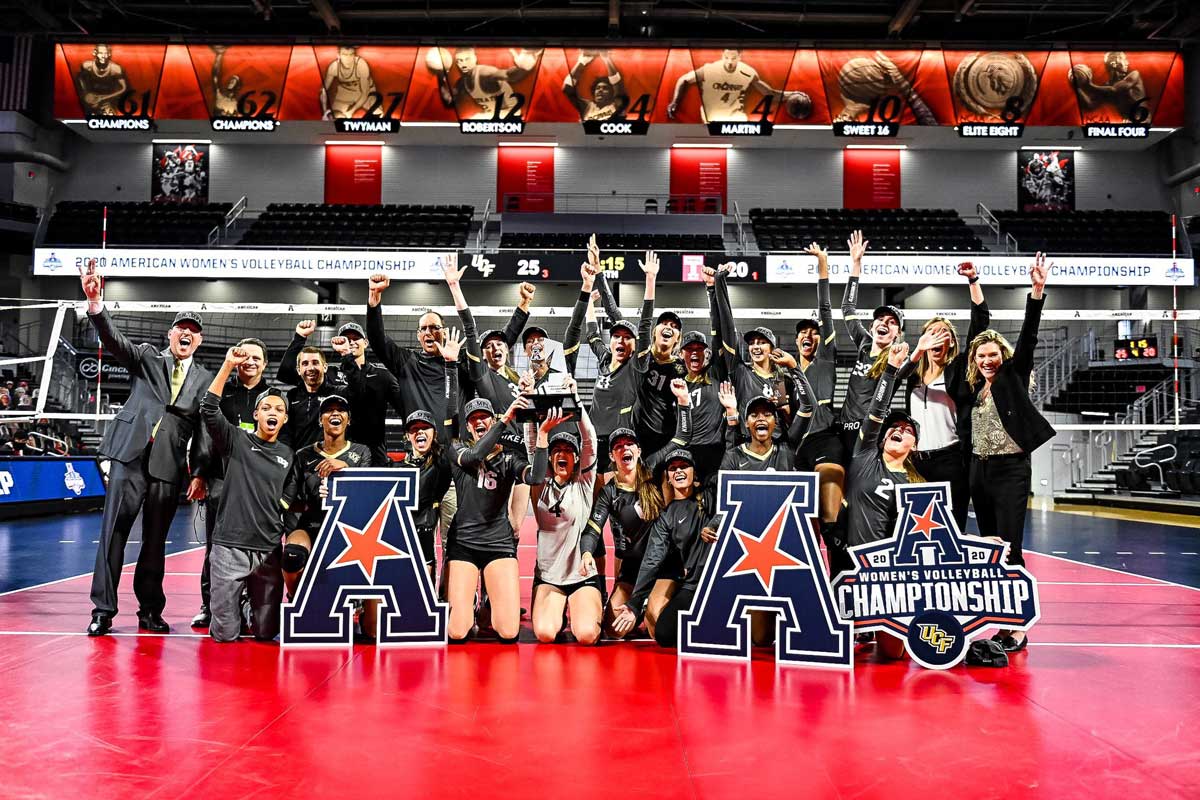 volleyball team poses on court with AAC trophy