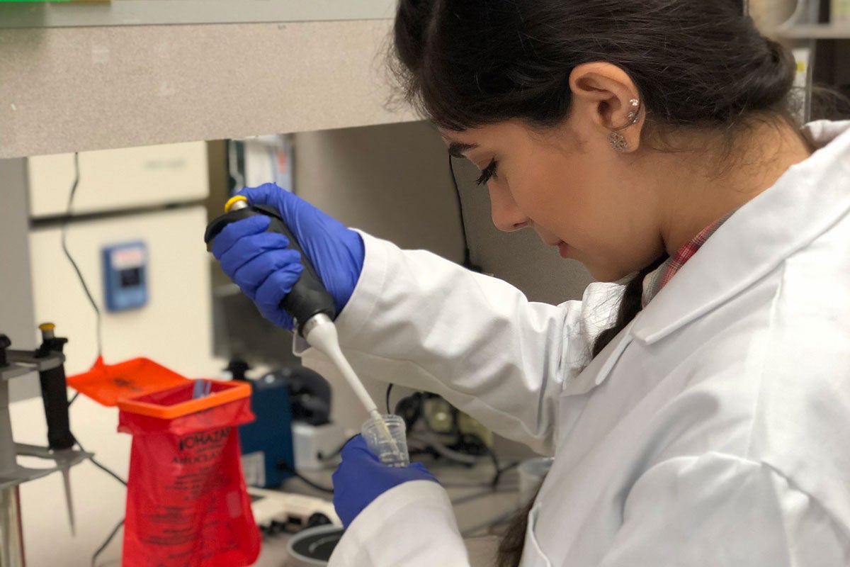 Woman in lab coat and blue gloves uses syringe in beaker