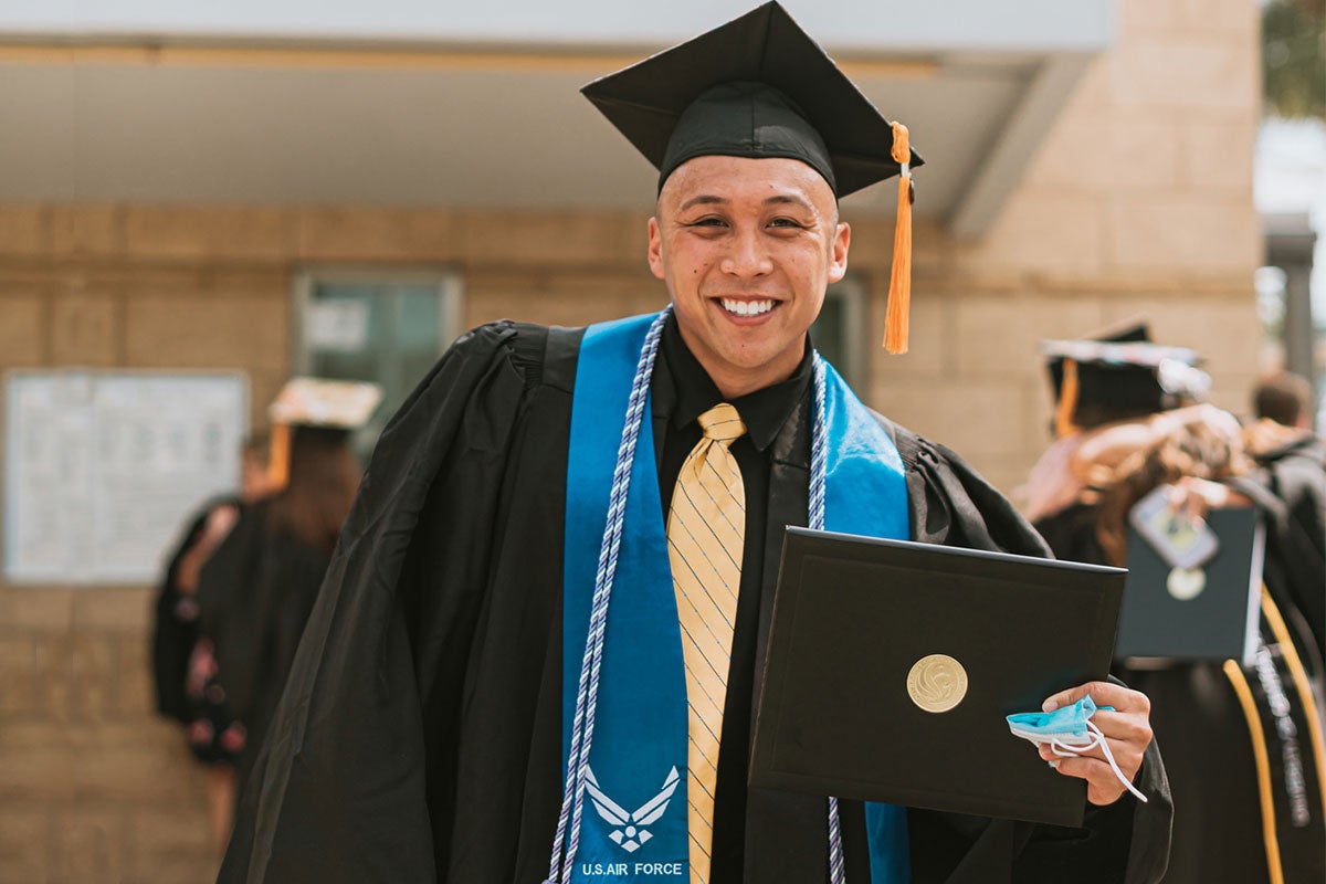 Male grad in cap and gown with blue Air Force stole, holds diploma