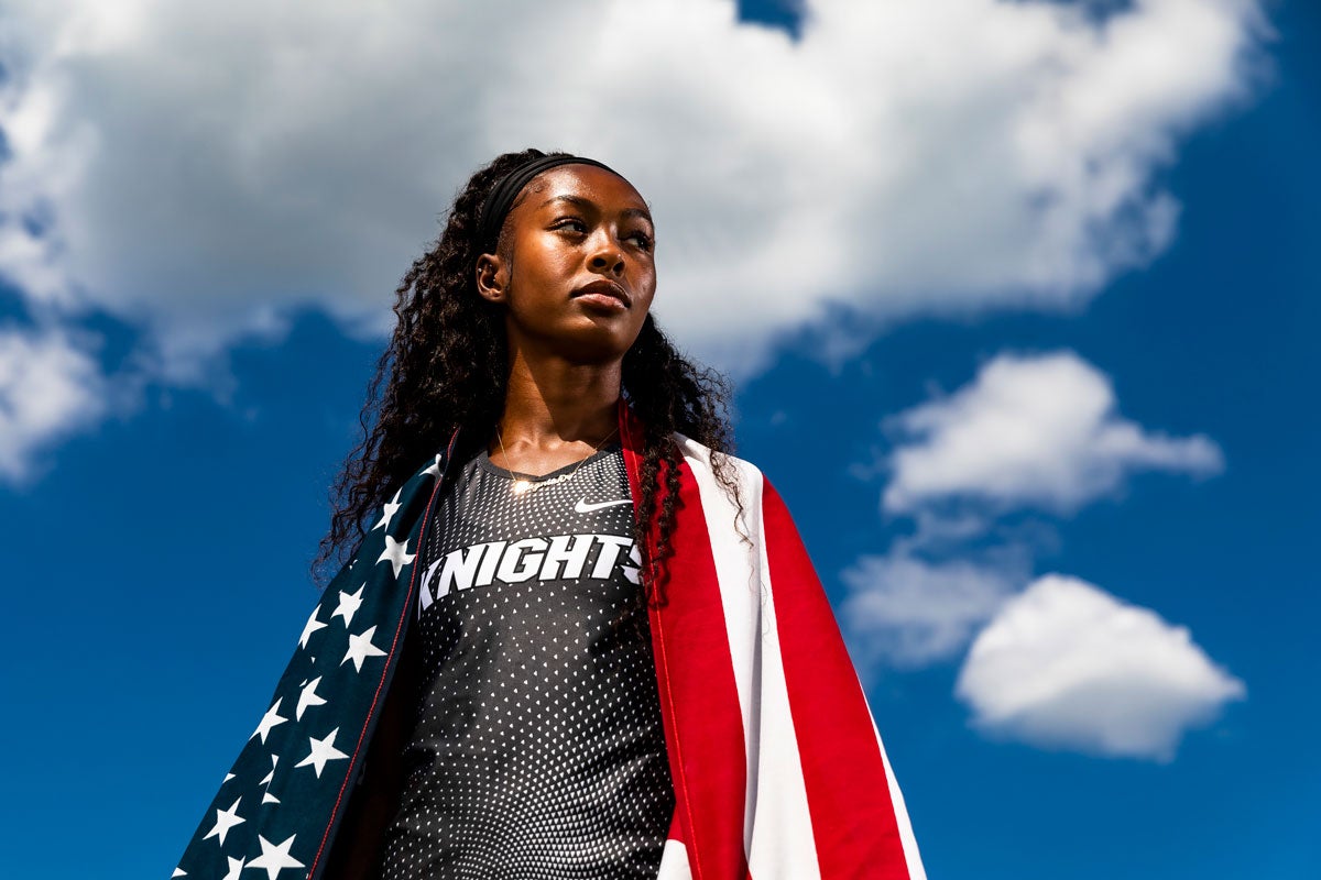 Rayniah Jones in gray Knights uniform with USA flag draped over her shoulders