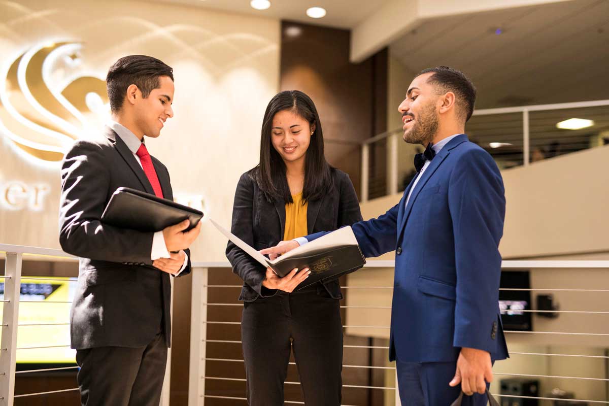 Two men and one woman dressed in business suits have a discussion while looking at binders