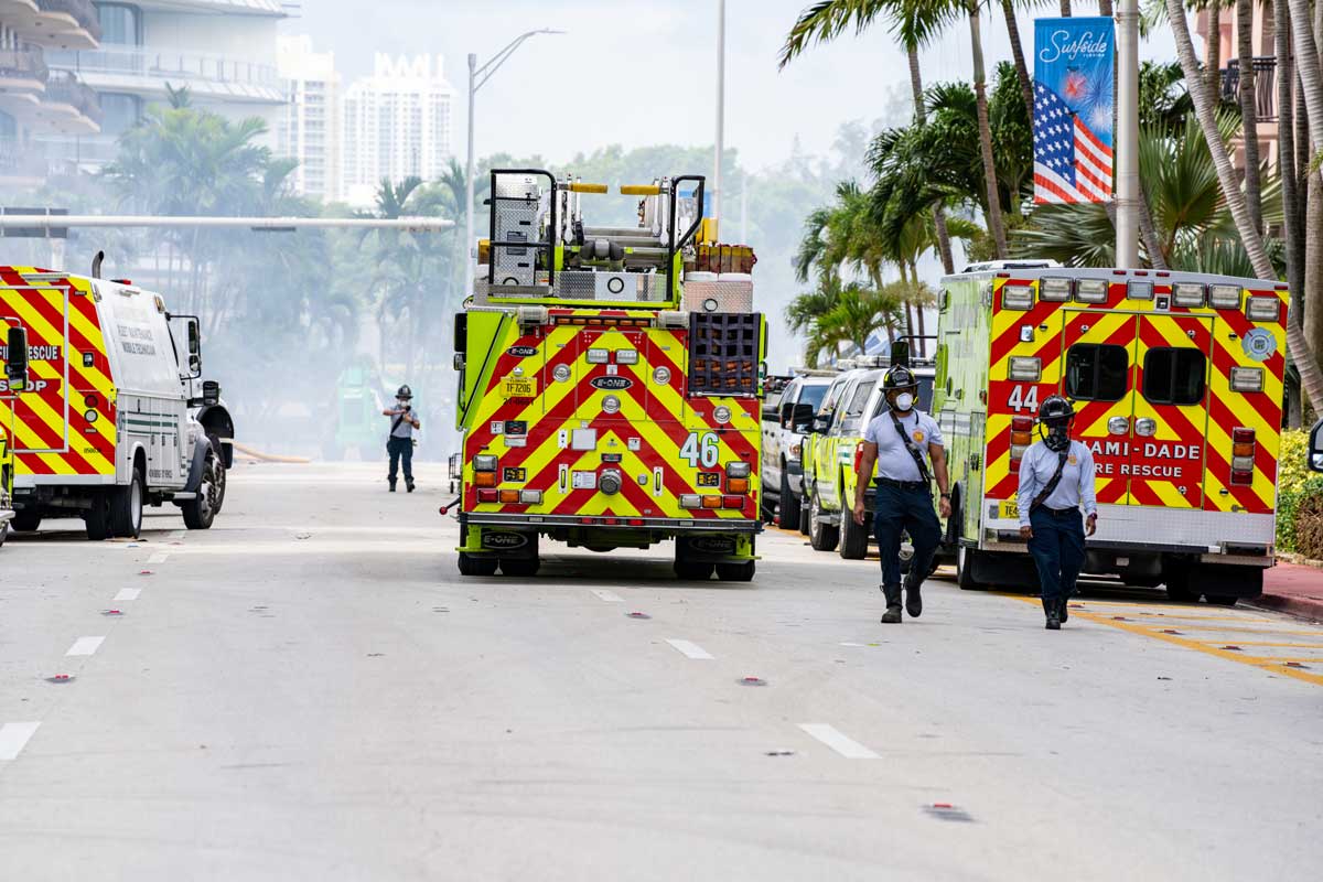 Miami Dade emergency response vehicles parked on dusty street with two first responders walking nearby