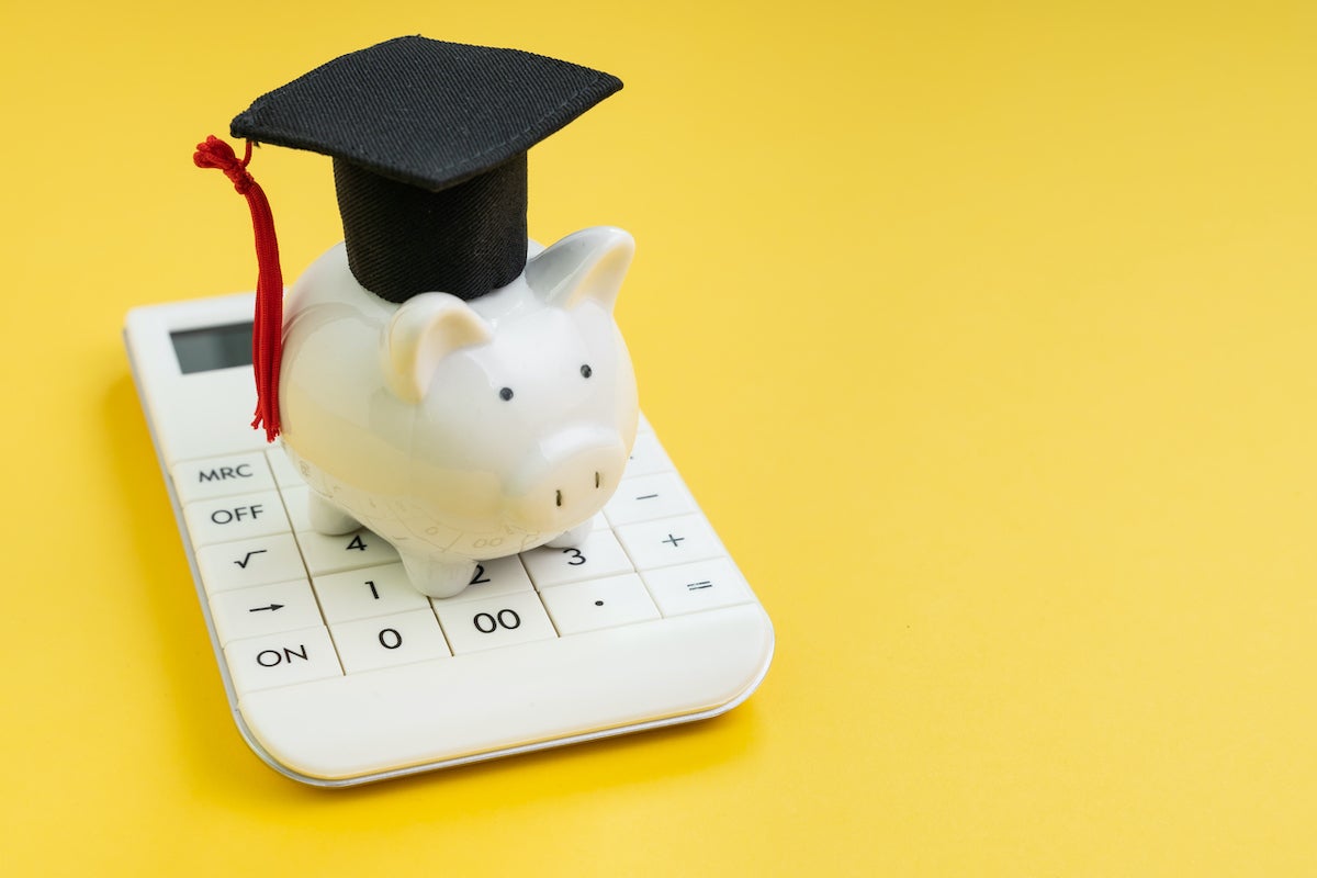 Student loan payment calculation, scholarship or saving for school and education concept, white piggy bank wearing graduation hat on calculator on yellow background with copy space. (Student loan payment calculation, scholarship or saving for school a