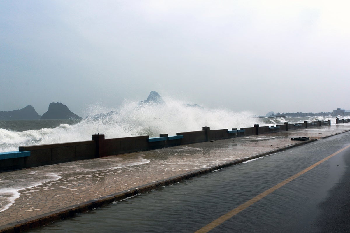 waves breaking against a wall with a street running by