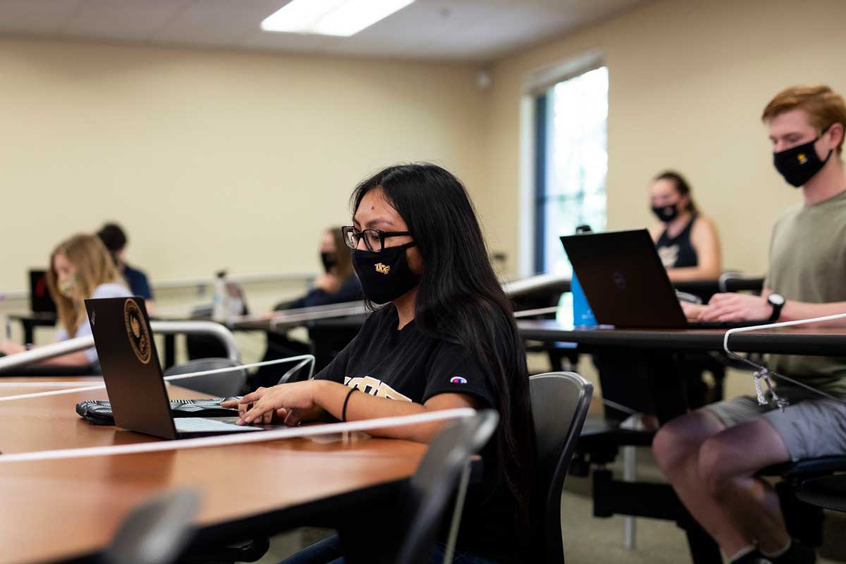 A group of students wearing masks sit at desks in lecture hall