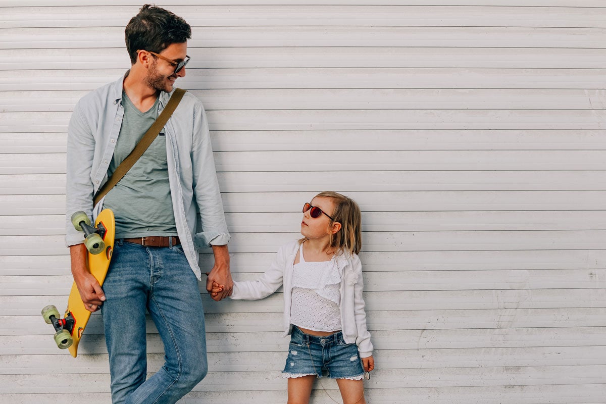 Dad holds skateboard while holding daughter's hand