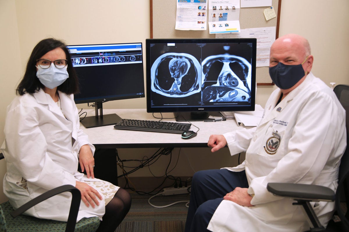 One woman and one man in lab coats sitting at a desk with x ray images on computer screens