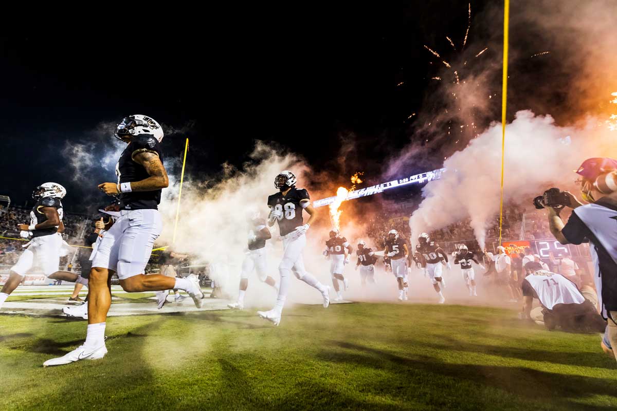 UCF football players run onto the field from locker room tunnel at night with fireworks shooting off
