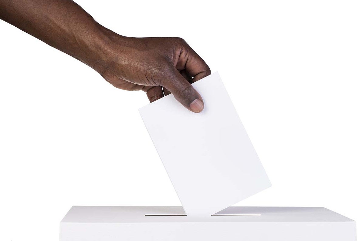 a hand dropping a ballot into a voting box