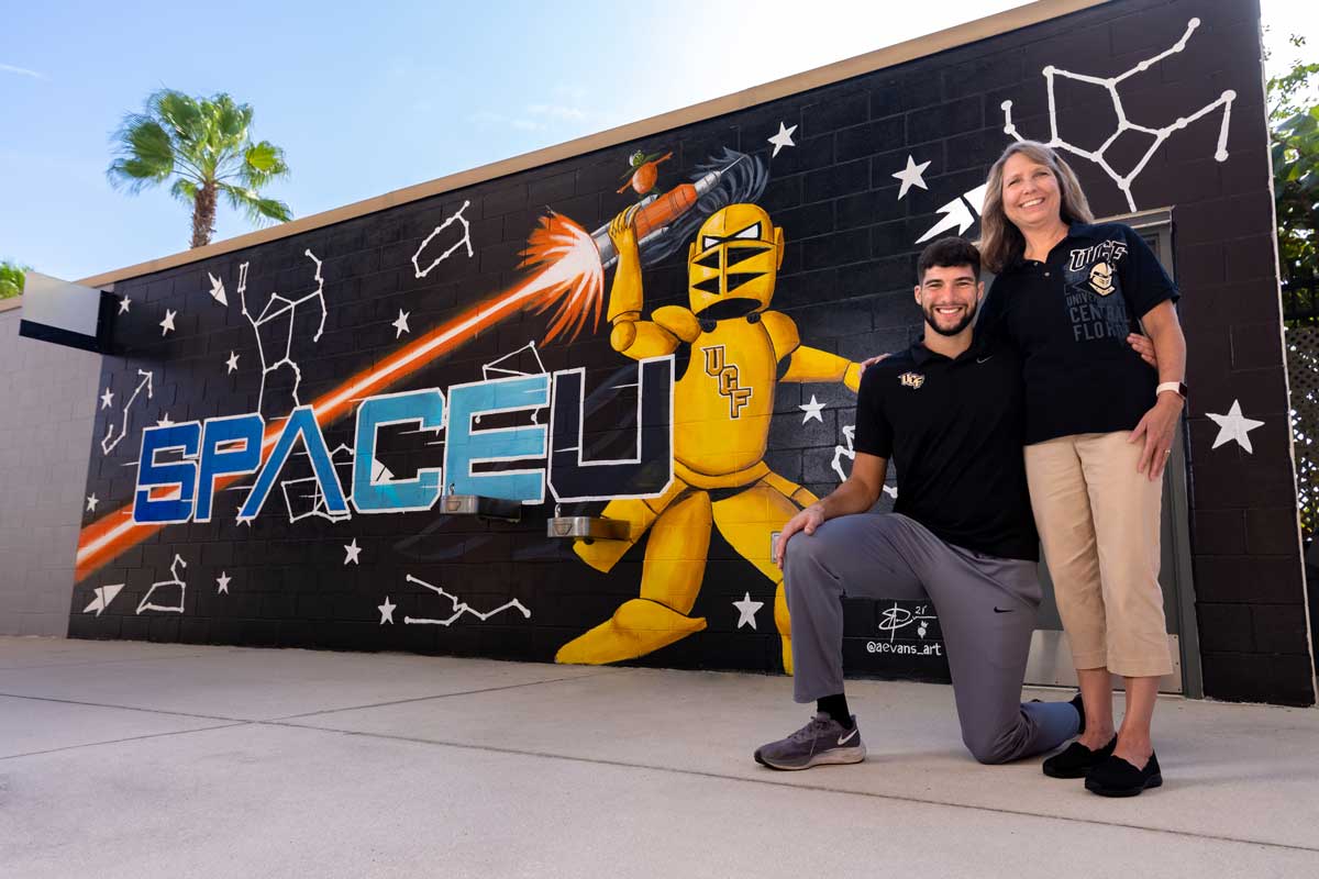 Stephen and Sharlene Martin stand in front of SpaceU mural that features Knightro holding a rocket/flare