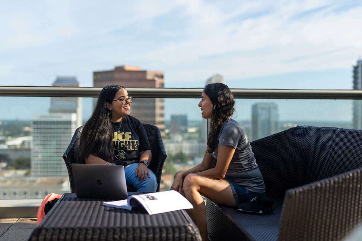 Two students sit outside with book and laptop on table