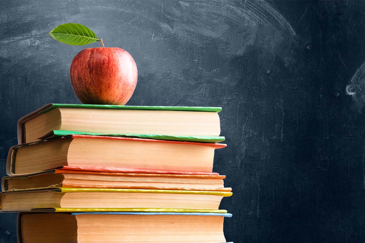 An apple sits on top of books with a chalkboard in the background