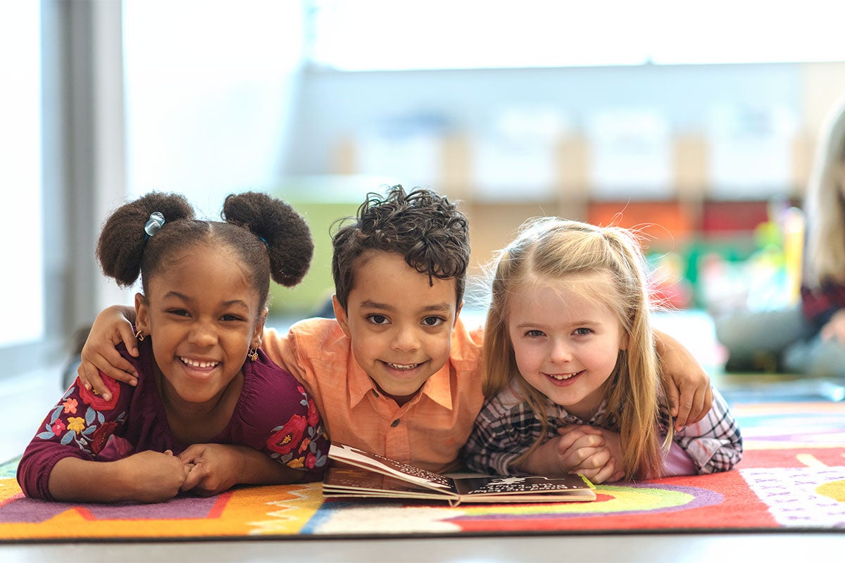 Three young children laying down and with a book.