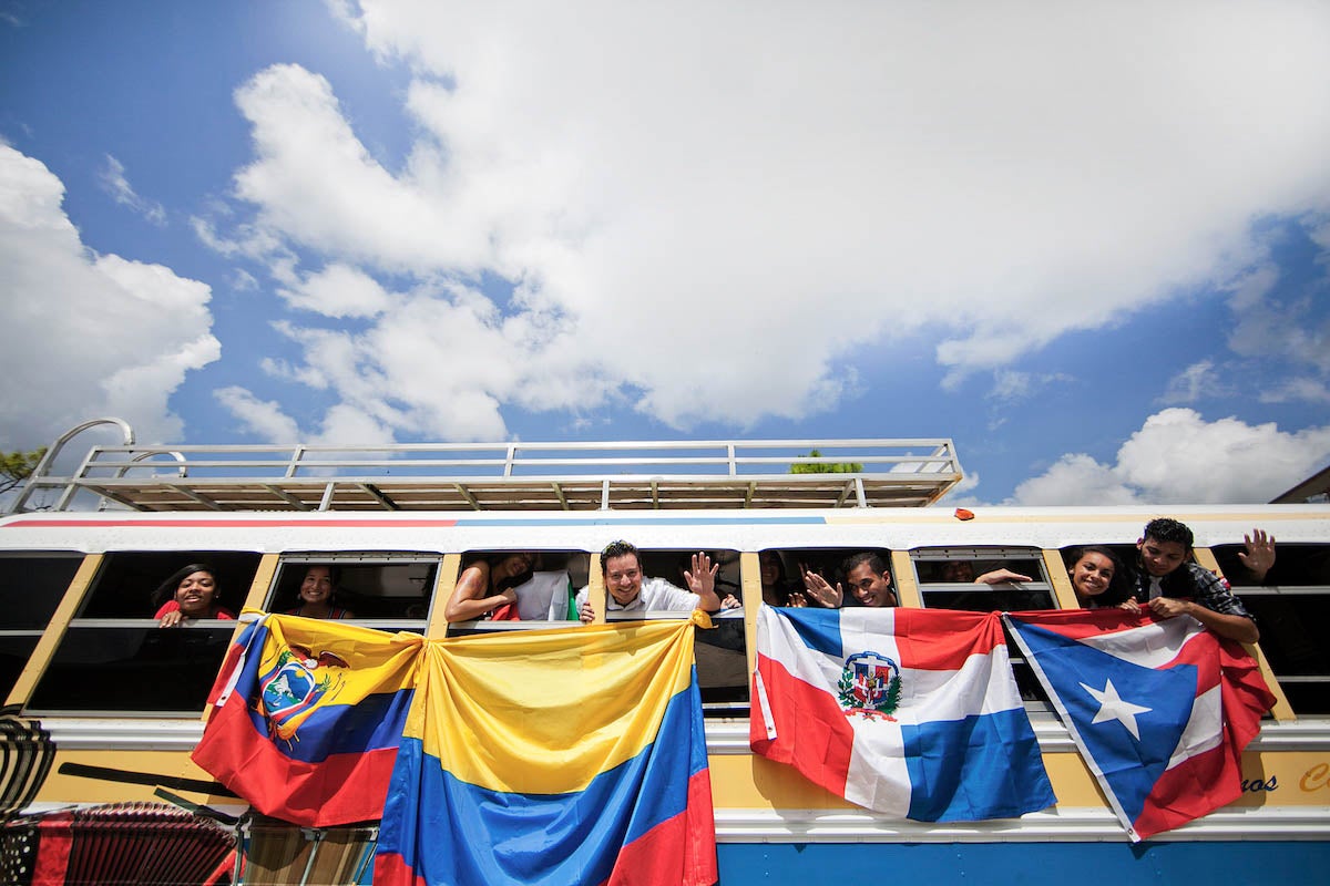 Students holding various Hispanic flags out of a bus