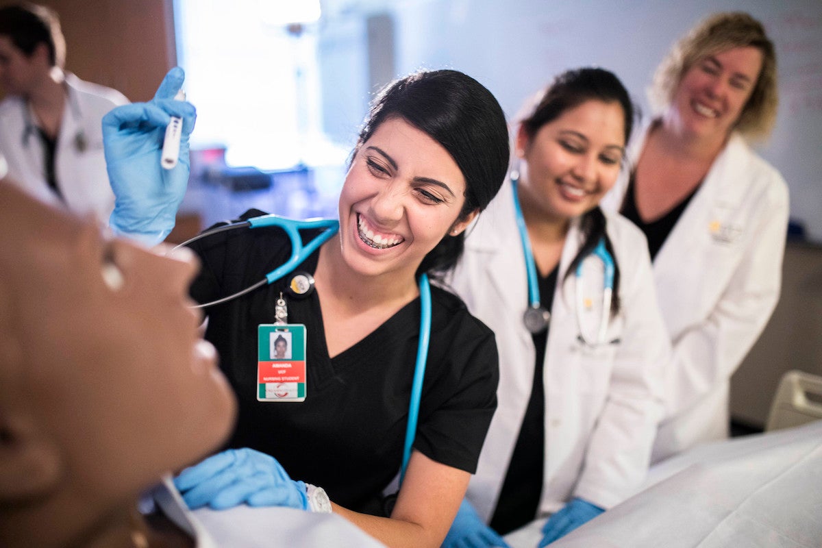 A nursing student examines a manikin while being supervised by faculty.