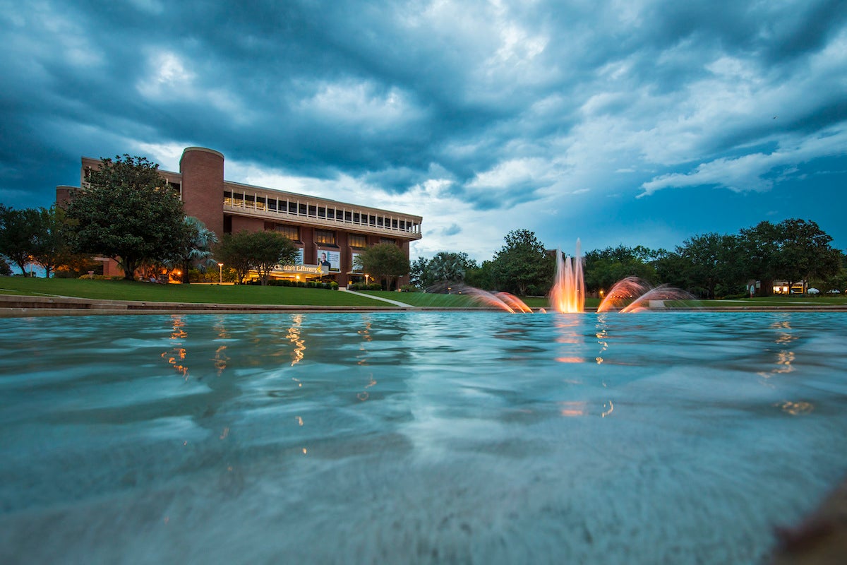 A fountain in the UCF reflecting pond with the John C. Hitt library in the background.