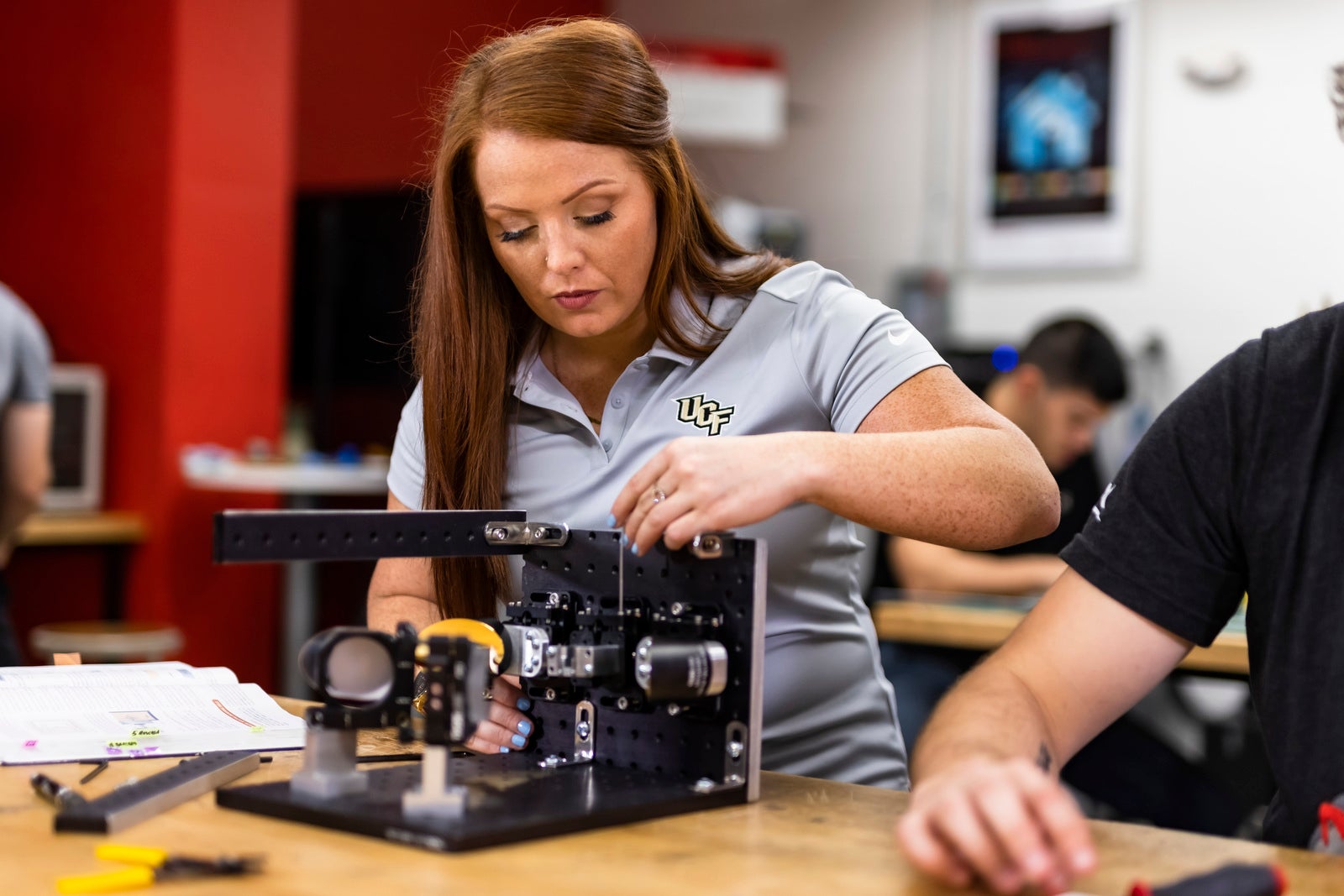 Woman in gray UCF polo tinkers with hardware on a wooden ab table