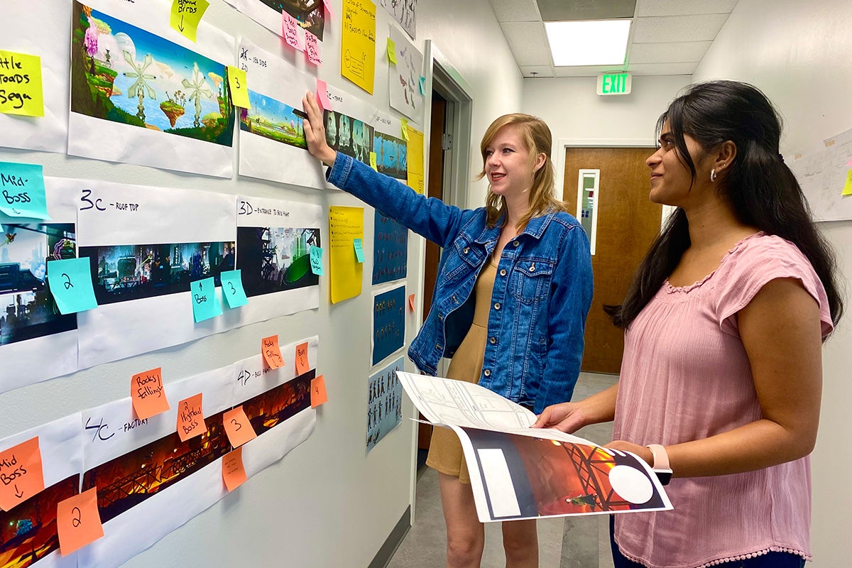 two ladies are looking at concept art on a wall