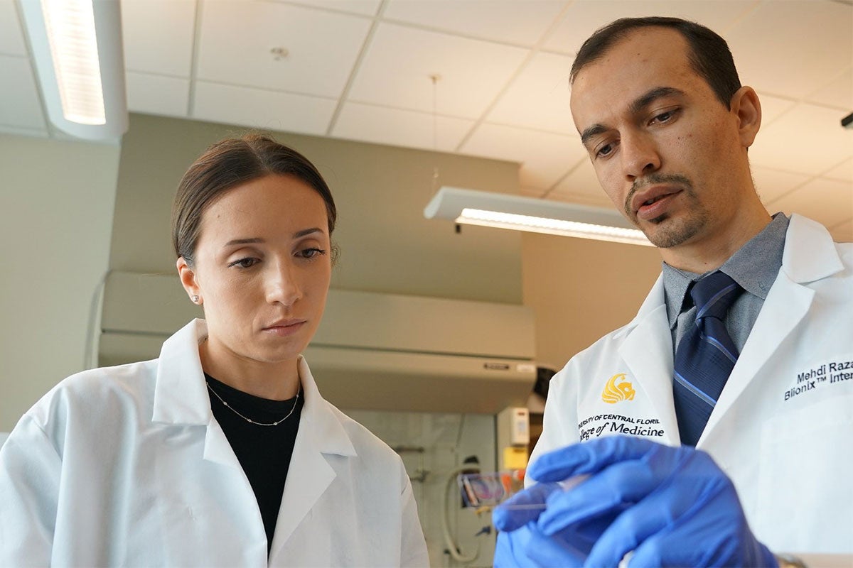 Two people wearing white coats examine a slide of tissue