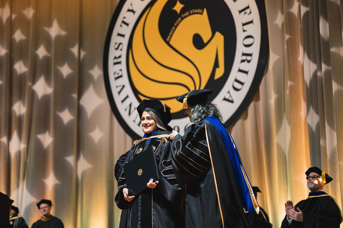 A doctoral student on a commencement stage with another woman
