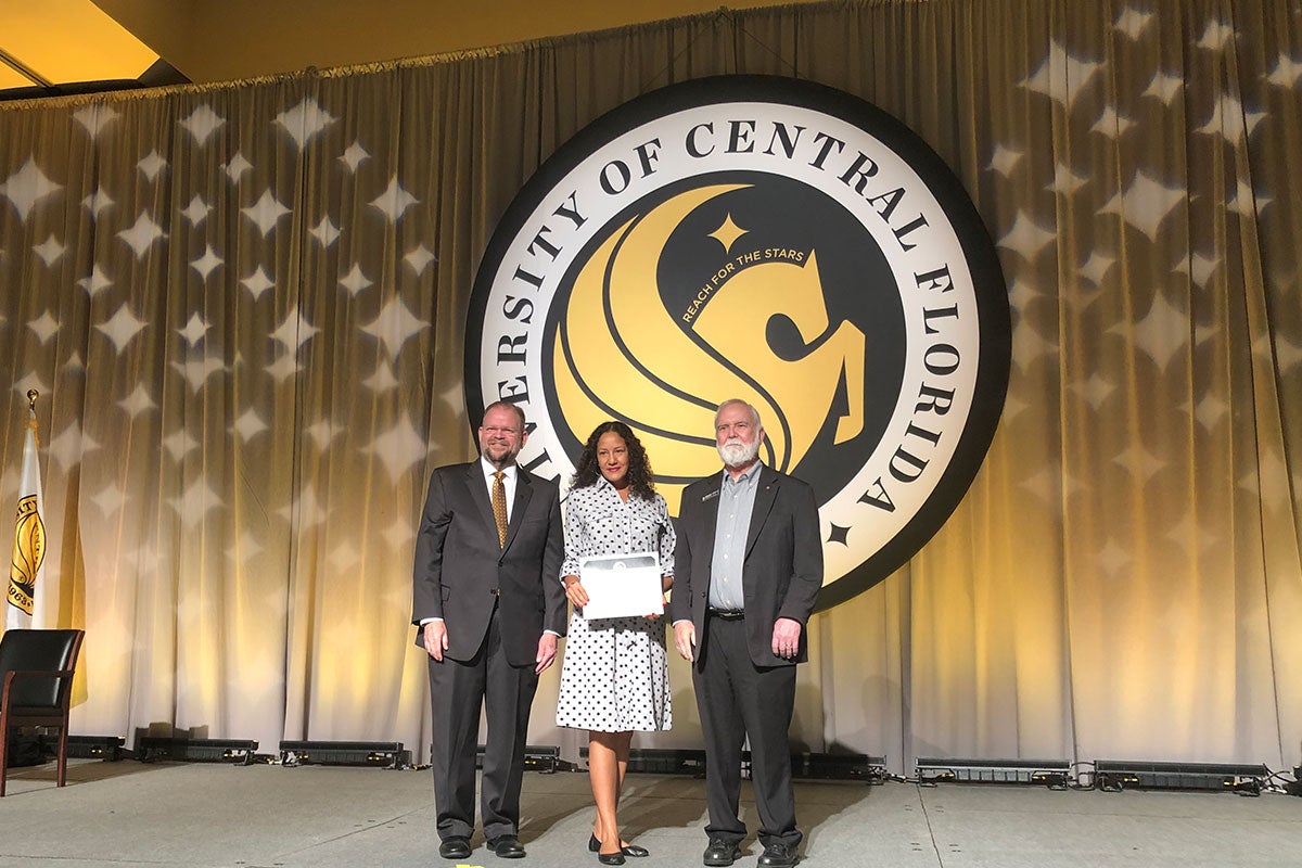 Alexander N. Cartwright and Michael D. Johnson stand on a stage with a UCF employee