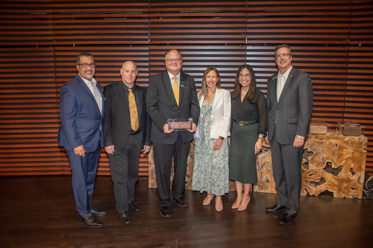 A group of six men and women pose for a photo while holding an award