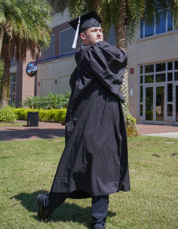 Luis Carrera wearing a cap and gown and posing with a gold club