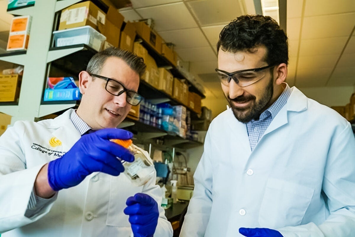 Two men wearing lab coats and gloves examine research materials