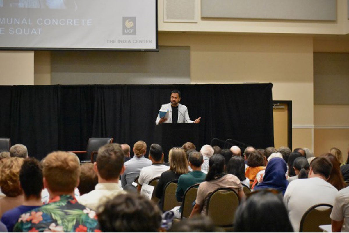 Kal Penn speaking at a podium in a room full of people