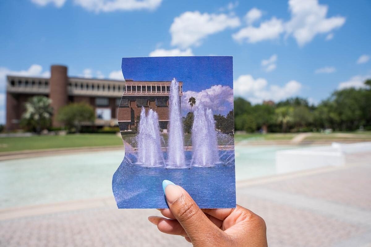 A person holds an old photo of the Reflecting Pond in front of the present day site.