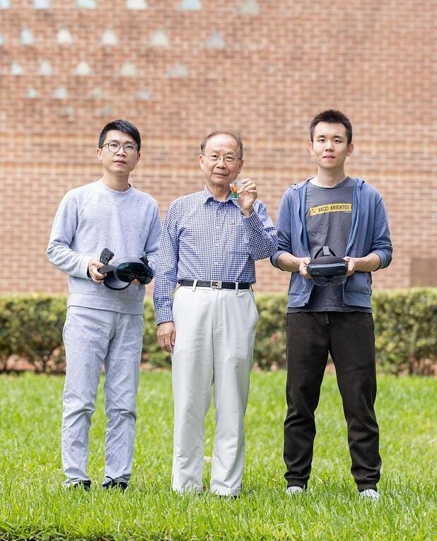 Shin-Tson Wu and doctoral students stand outside UCF's College of Optics and Photonics while holding VR headsets and other tech.