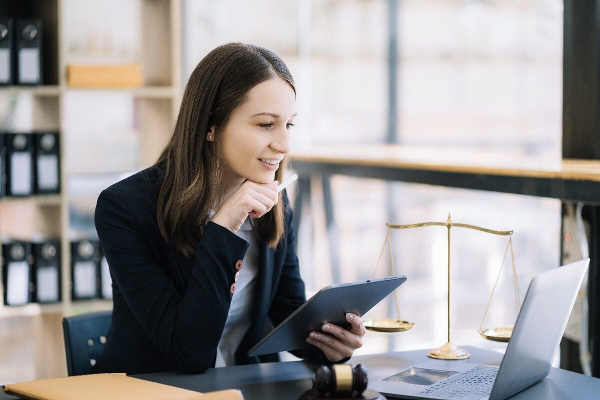 A lady is looking at a laptop with some scales, which represent justice, in the background