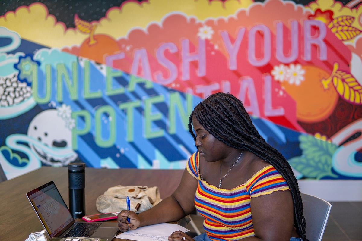 A student using a laptop in front of a mural that says "Unleash your potential"
