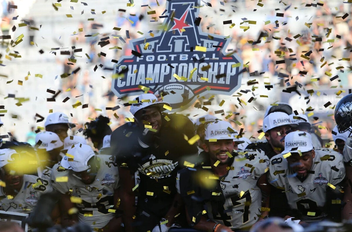 Football players hold an AAC championship sign as confetti rains down